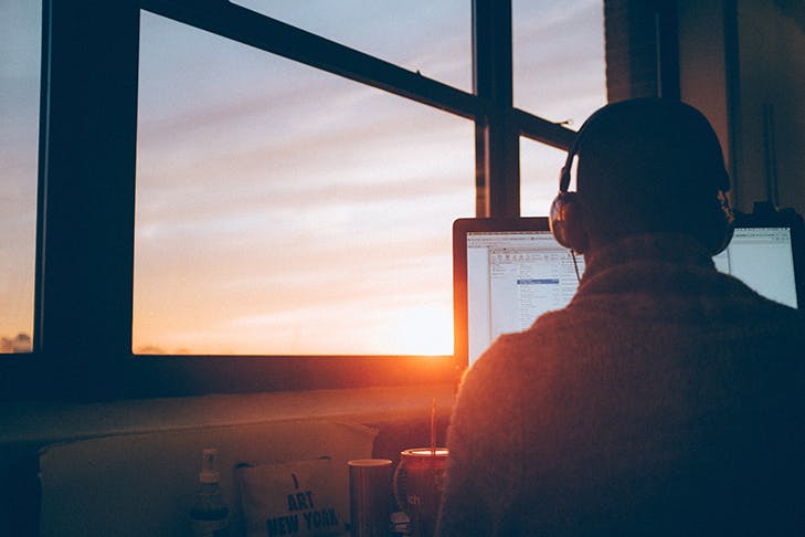 A person working on a computer by an office window. The afternoon sun is shining through.